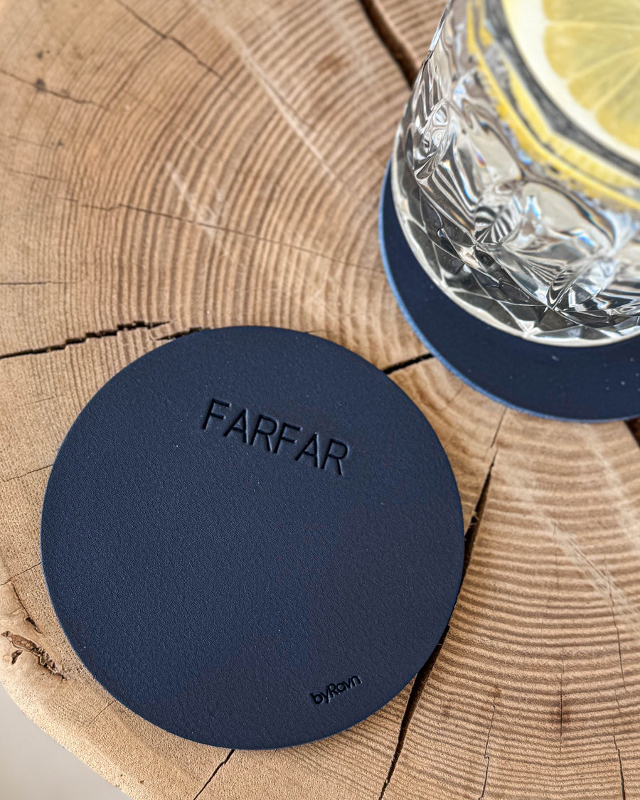 MOKKA runt glasunderlägg i mörkblått läder med gravyren "Farfar" på träskiva vid kristallglas med citron