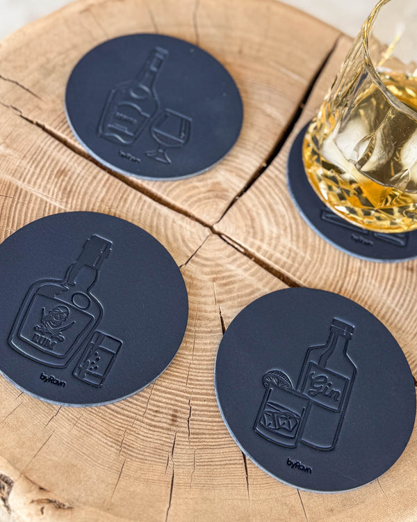 MOKKA glasunderlägg i mörkblått läder med spritmotiv cognac, rom och gin på träskiva vid kristallglas med whisky och is