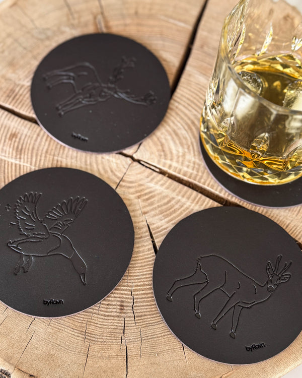 MOKKA jakt-glasunderlägg i mörkbrunt läder präglade med gräsand, råbock och kronhjort på träskiva vid whiskyglas
