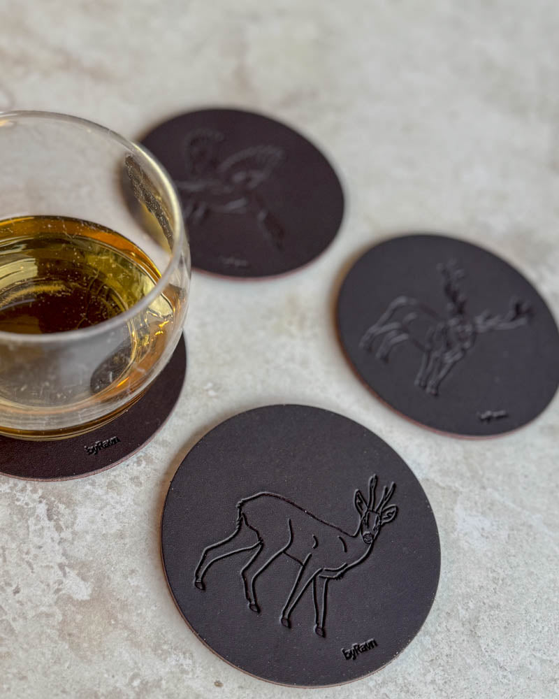 MOKKA jakt-glasunderlägg i mörkbrunt läder präglade med råbock, gräsand och kronhjort på ljust bord vid glas whisky