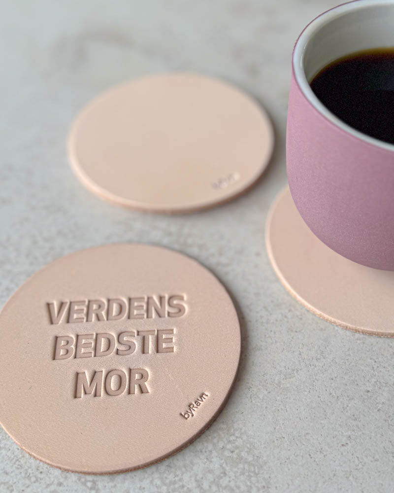 MOKKA glasunderlägg i naturfärgat läder präglade "Verdens bedste mor" på ljust bord med rosa kaffekopp