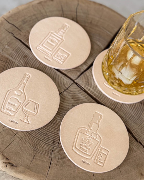 MOKKA sprit-glasunderlägg i naturfärgat läder präglade med cognac, rom och whisky på träskiva vid glas med whisky och is