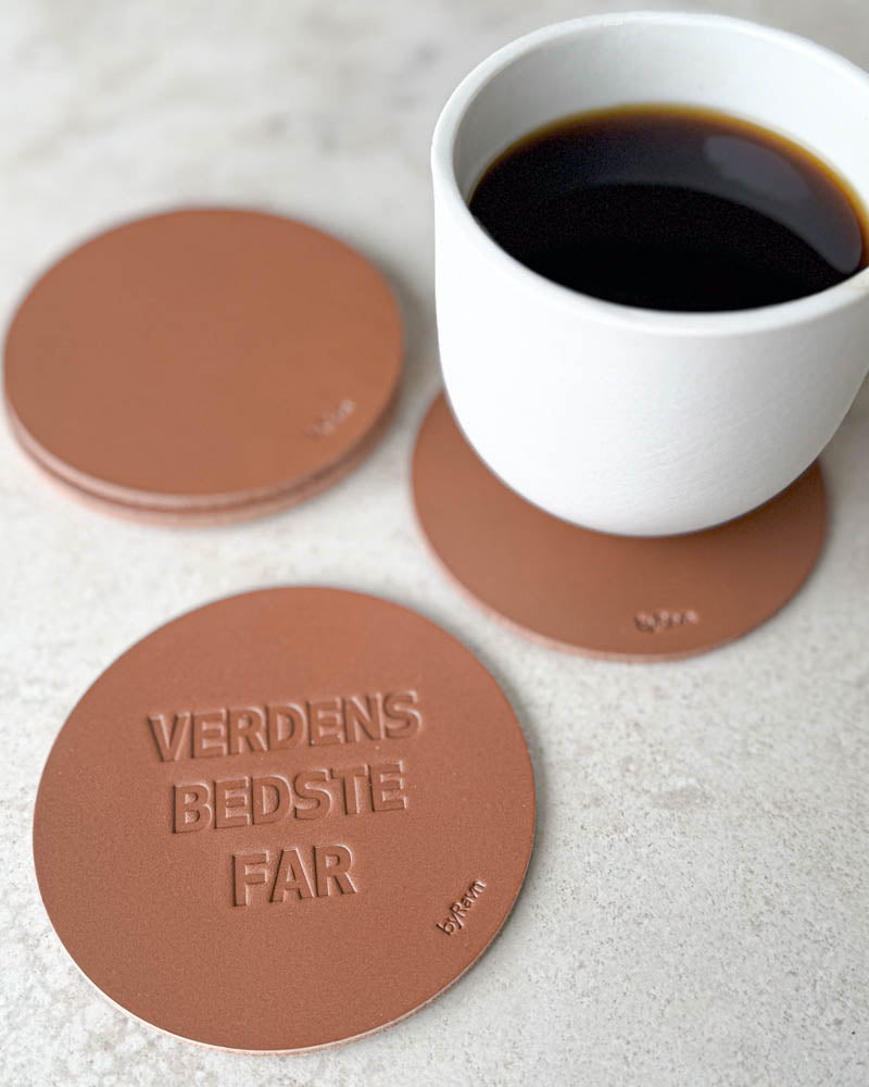 MOKKA glasunderlägg i cognacfärgat läder präglade "Verdens bedste far" på ljust bord med vit kaffekopp