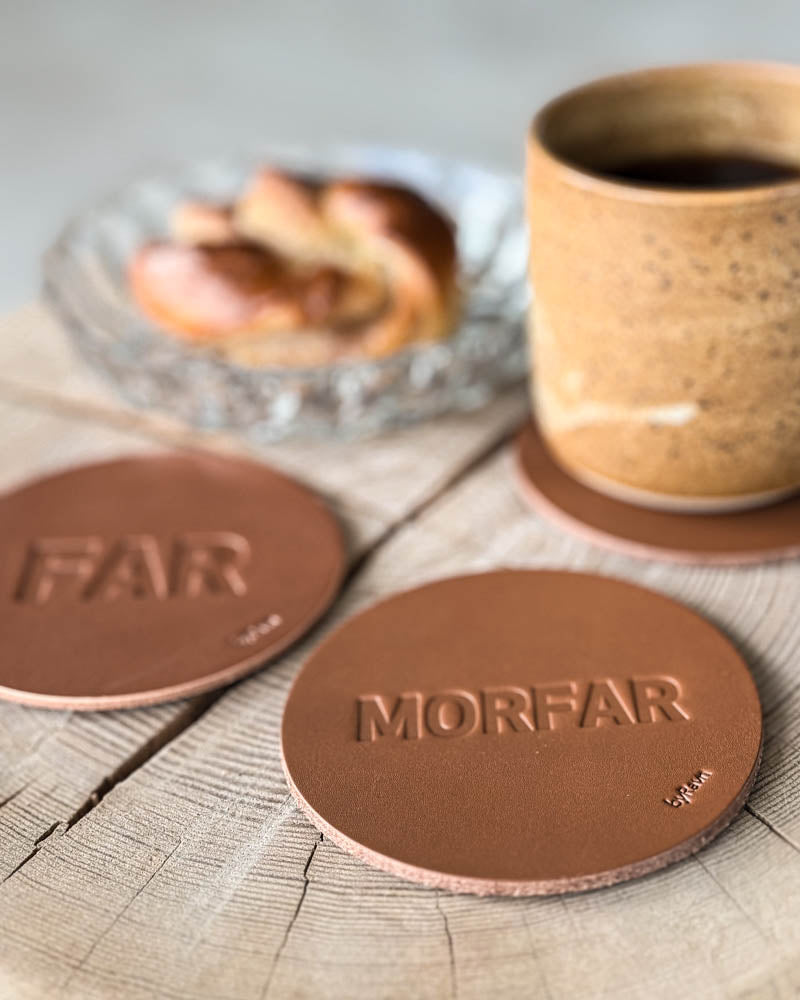 MOKKA glasunderlägg i cognacfärgat läder präglade "Far" och "Morfar" på träskiva med kaffekopp och kanelbulle på glasfat