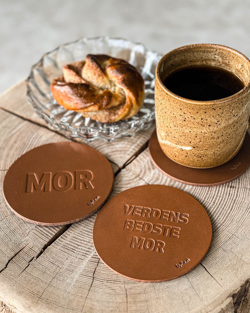 MOKKA glasunderlägg i cognacfärgat läder präglade "Mor" och "Verdens bedste mor" på träskiva med kaffekopp och kanelbulle
