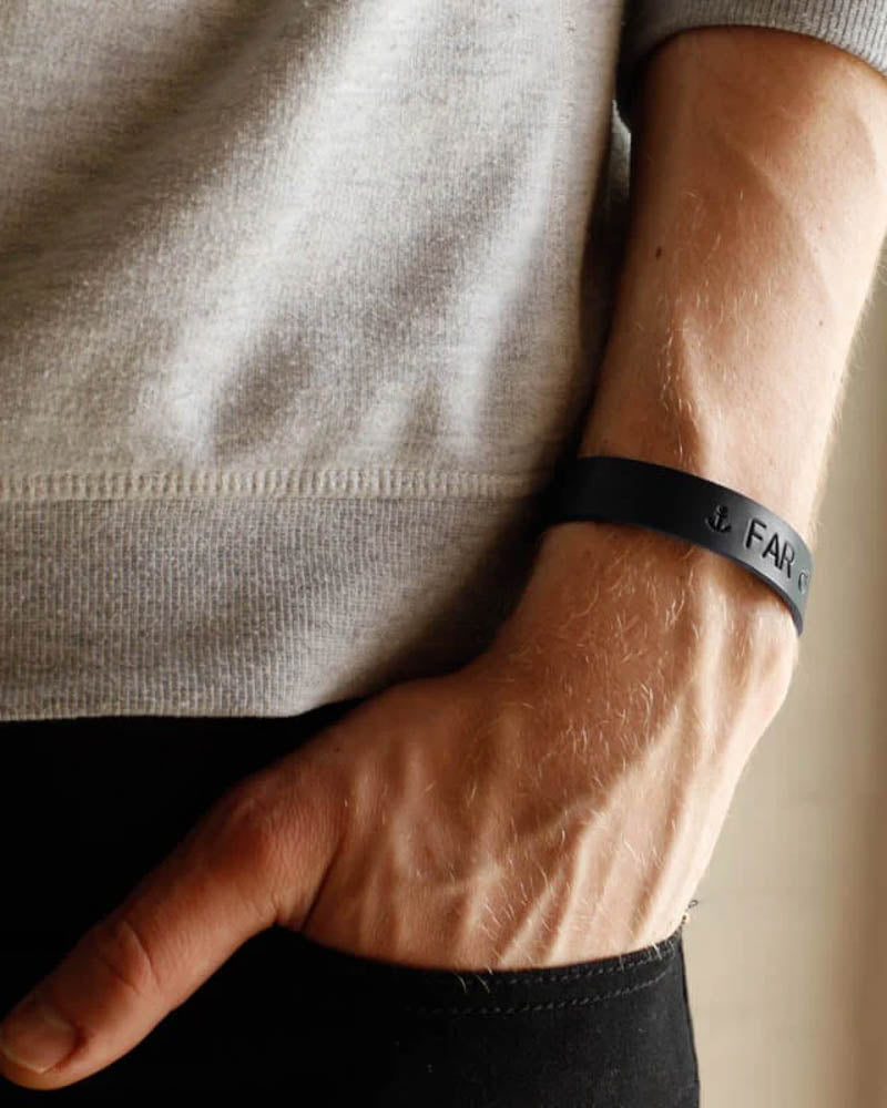 MONO läderarmband i svart läder med ankarsymbol och gravyren "Far" runt handleden, hand i byxfickan