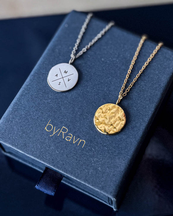 MOON X halsband i silverfärgat stål med kors och initialerna "M V S A" graverade, med hamrat guldpläterat mynt på byRavn smyckesask
