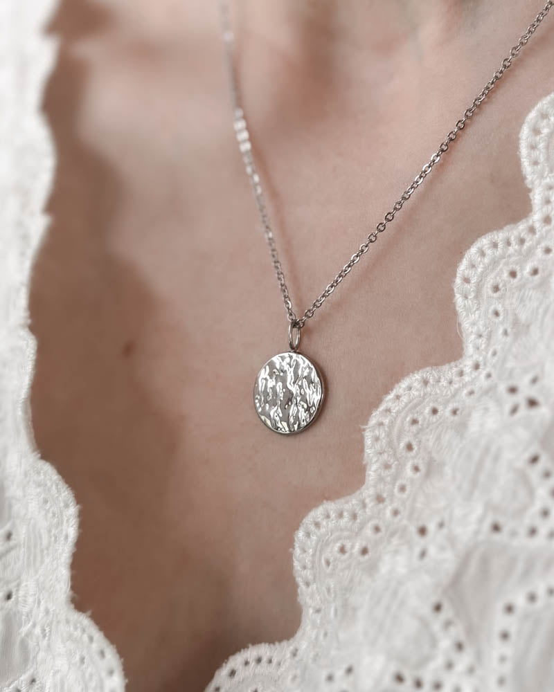 MOON QUOTE halsband i silverfärgat rostfritt stål med hamrat runt mynt vänt utåt, buret runt halsen över vit spetstopp