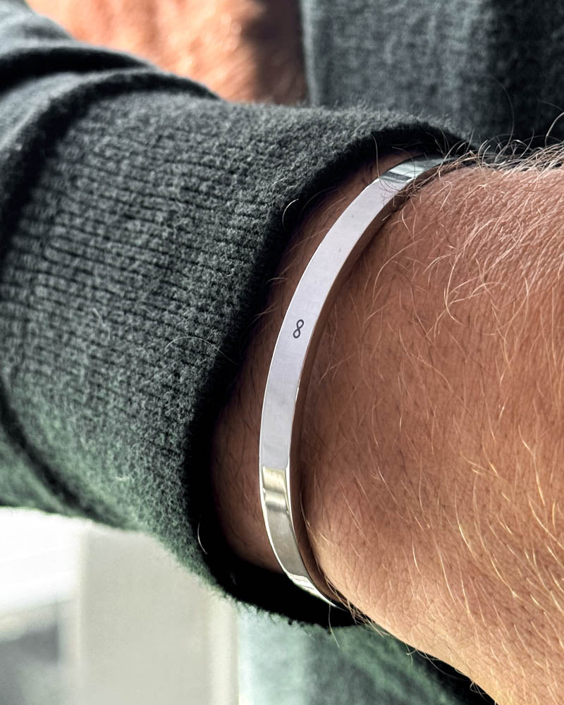 MARS armband i silverfärgat rostfritt stål med oändlighetstecken ∞ graverat runt handleden, mörkgrön stickad tröja