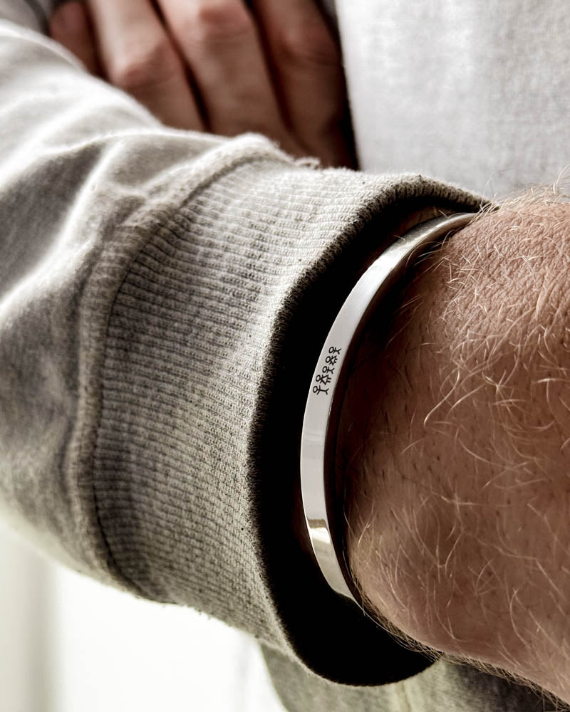 MARS STICK armband i silverfärgat rostfritt stål med graverad tändsticksfamilj runt en mans handled, ljusgrå sweatshirt