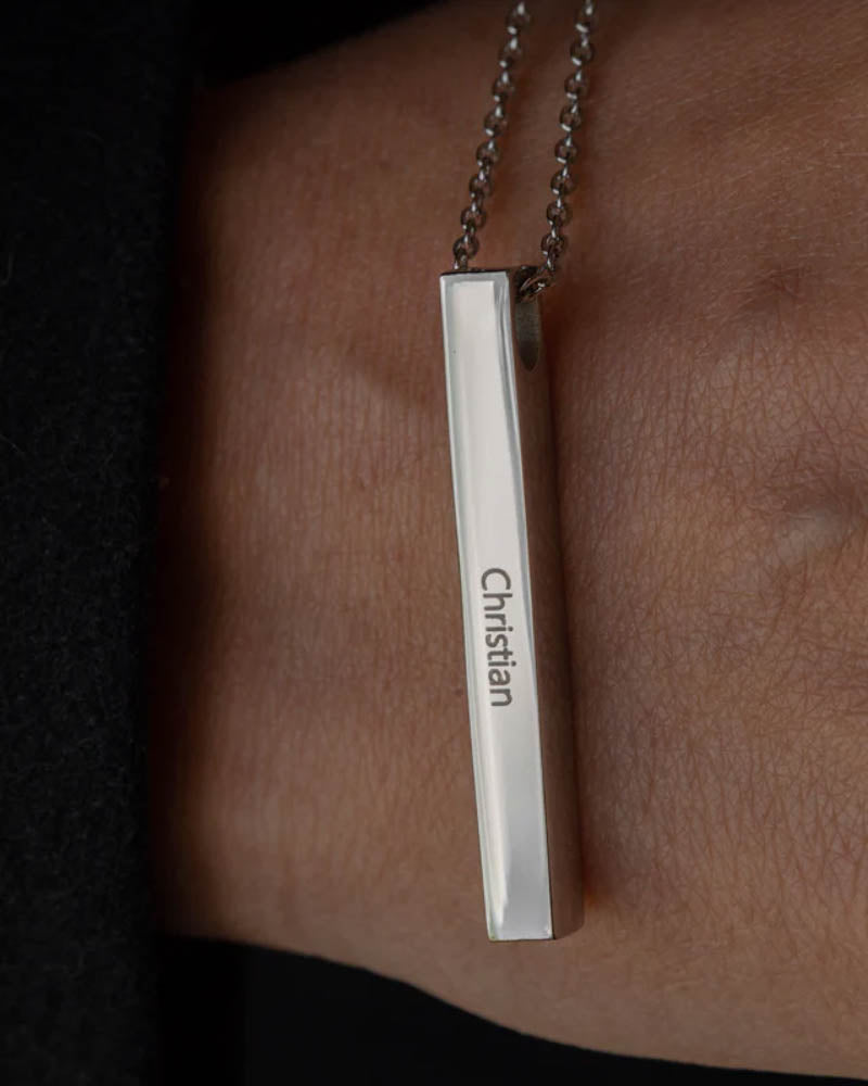 NEO namnhalsband i silverfärgat rostfritt stål med namnet "Christian" graverat på avlång stav, buret runt halsen över svarta kläder