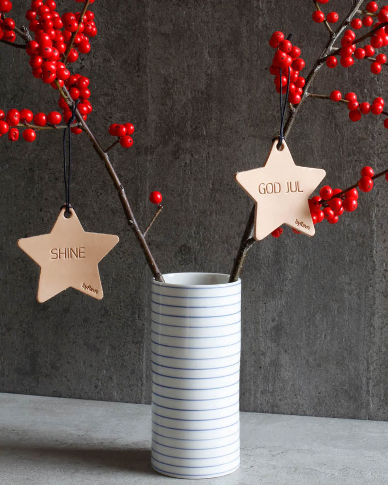 NORTH julstjärnor i naturfärgat läder med gravyrerna "Shine" och "God jul" hängda på kvistar med röda bär i randig vas