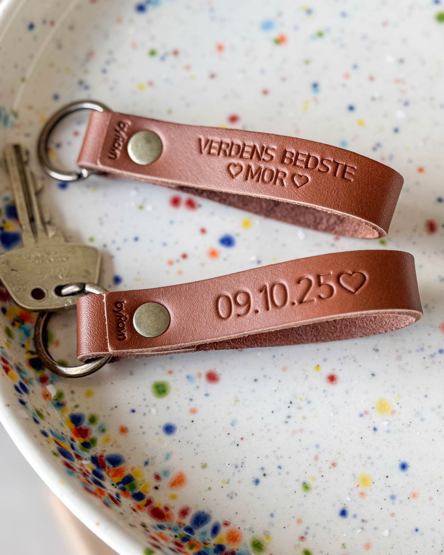 RAVN nyckelringar i cognac läder med gravyren "Verdens bedste mor" och datumet "09.10.25" ♡ i prickig keramikskål med nycklar