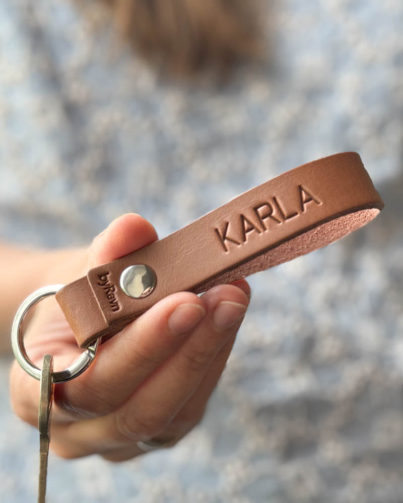 RAVN nyckelring i cognac läder med namnet "Karla" graverat, hålls i handen