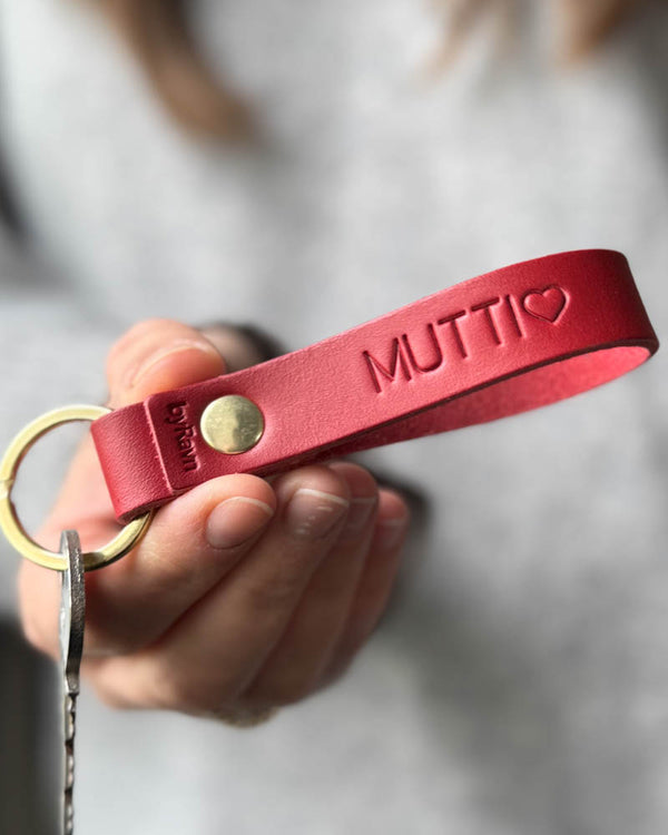 RAVN nyckelring i rött läder med personlig gravyr "Mutti" ♡ och mässingsnit, hålls i handen med nyckel