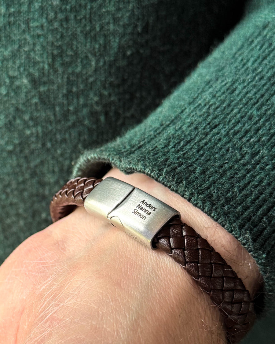 RAY läderarmband i mörkbrunt flätat läder med namnen "Anders, Nanna, Simon" graverade på stållåset, buret till grön stickat