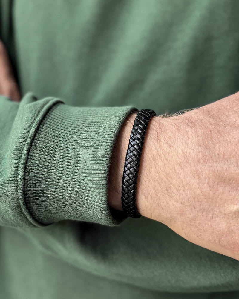 RAY läderarmband i svart flätat läder buret runt en mans handled, grön sweatshirt