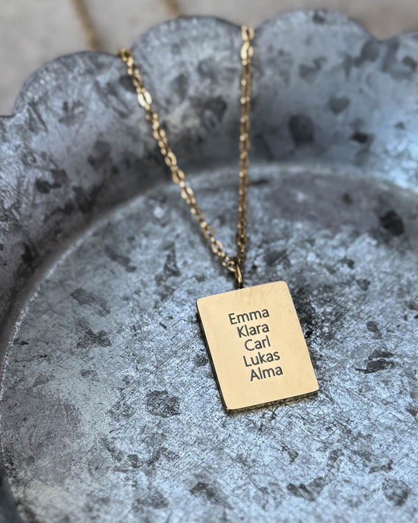 RAZ namnhalsband i guldpläterat stål med namnen "Emma Klara Carl Lukas Alma" graverade på rektangulär bricka, på zinkfat med vågig kant