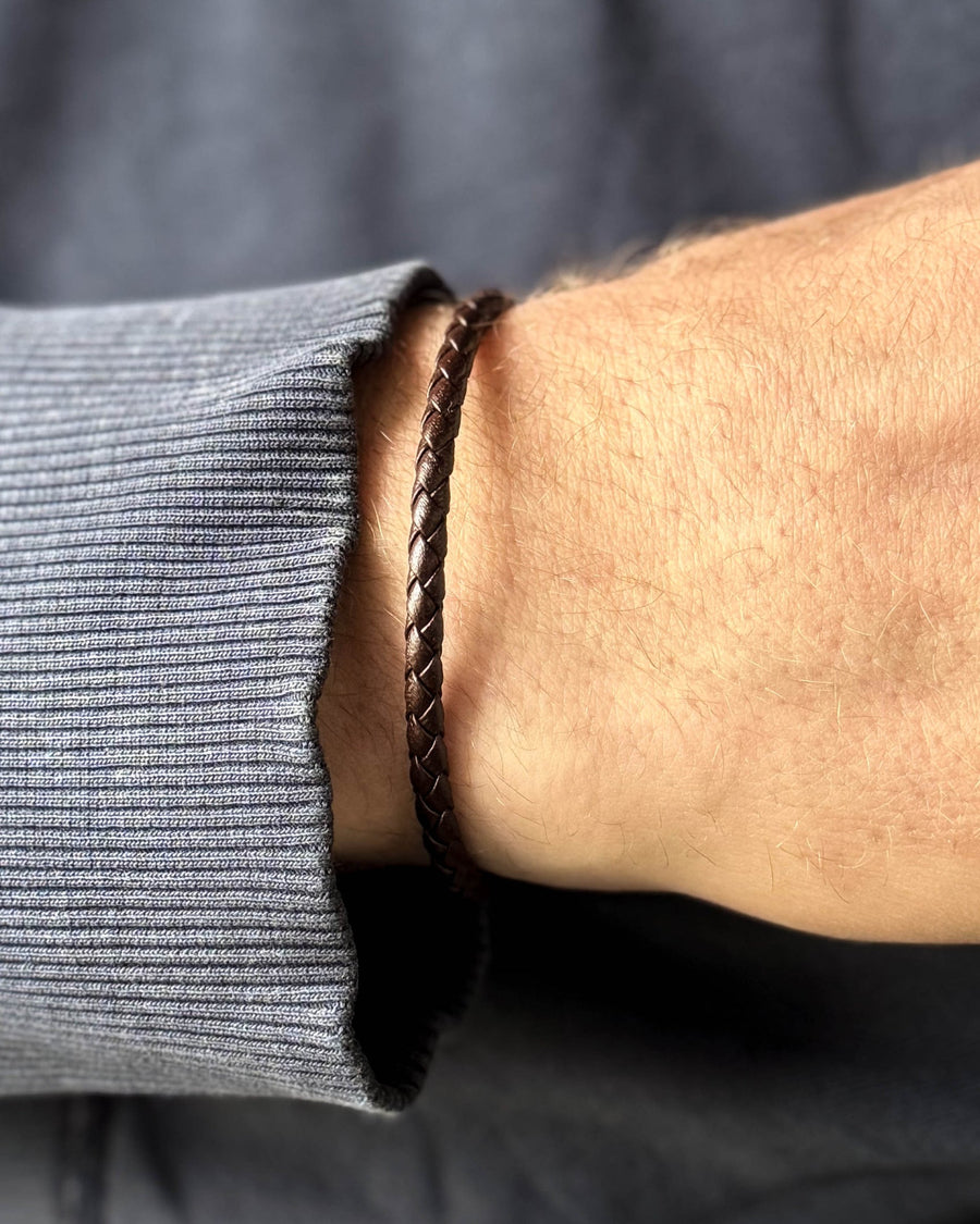 RIO läderarmband i mörkbrunt flätat läder runt en mans handled, blågrå sweatshirt