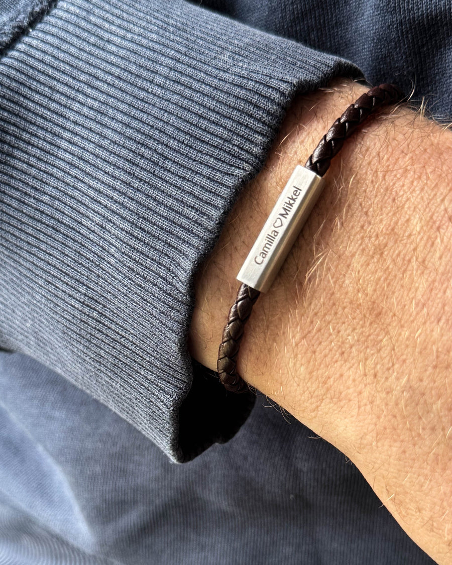 RIO läderarmband i mörkbrunt flätat läder med "Camilla ♡ Mikkel" graverat på stållåset, buret runt handleden