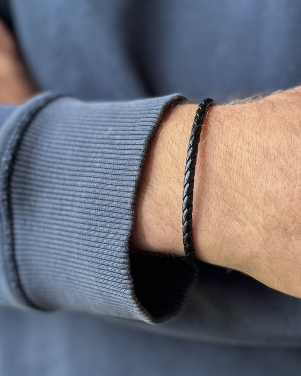 RIO läderarmband i svart flätat läder buret runt en mans handled, blågrå sweatshirt