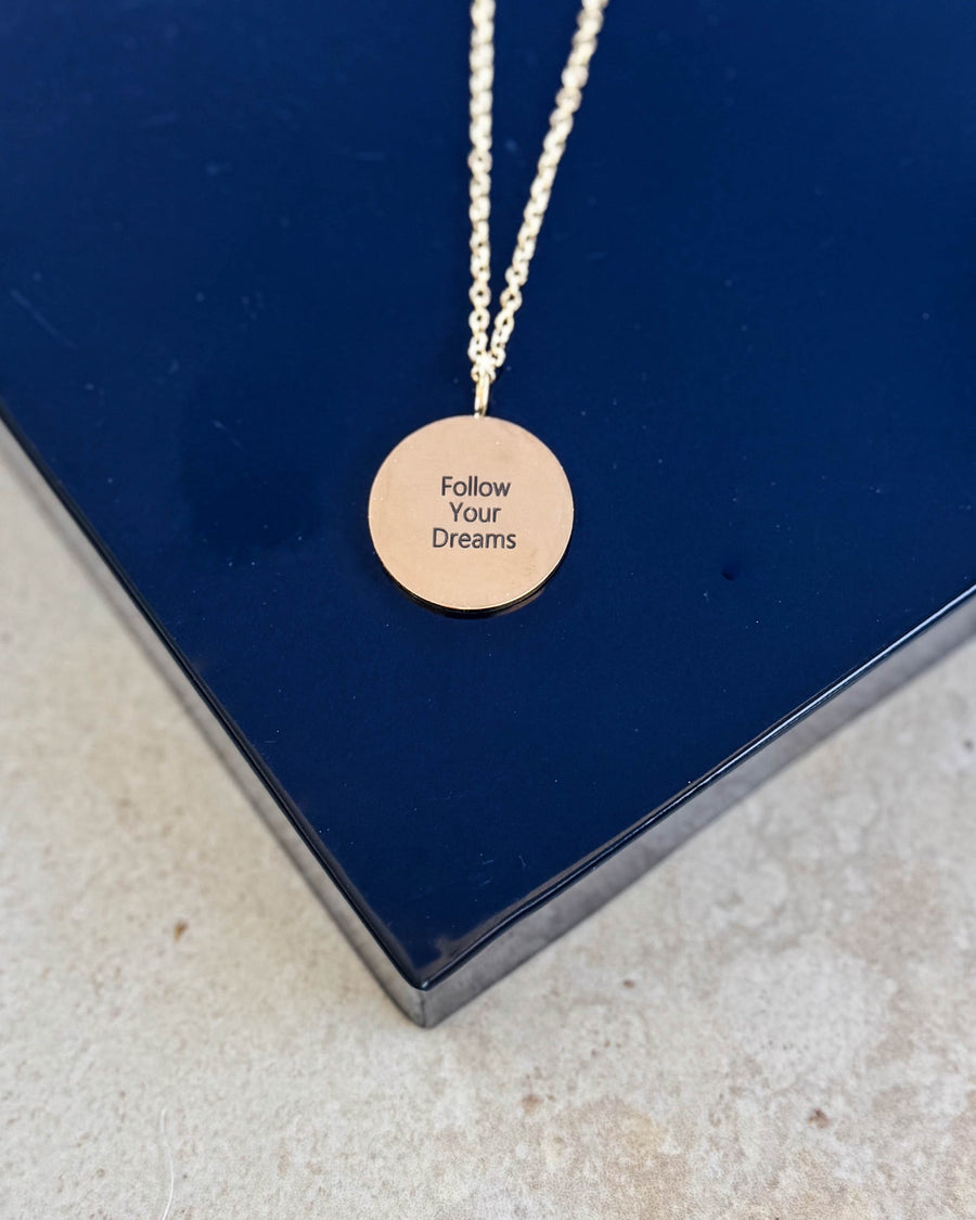 SIA QUOTE halsband i guldpläterat stål med gravyren "Follow your dreams" på runt hänge, på mörkblå ask