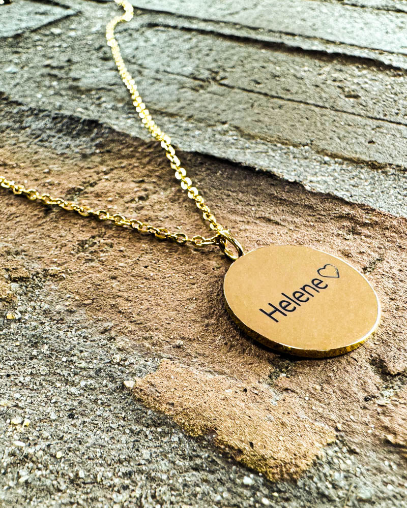 SIA NOTE namnhalsband i guldpläterat stål med namnet "Helene" ♡ graverat, liggande på tegelvägg