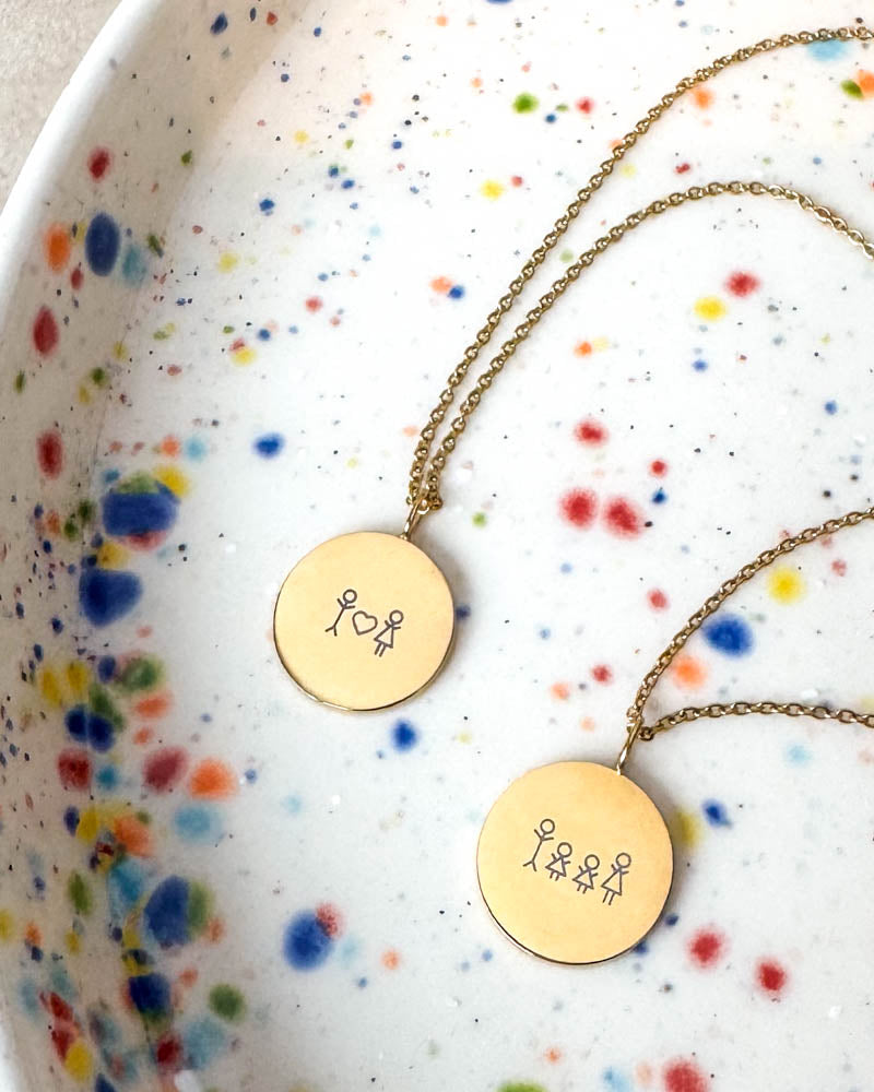 SIA STICK halsband i guldpläterat stål med tändstickspar med hjärta och tändsticksfamilj graverade, på prickigt keramikfat