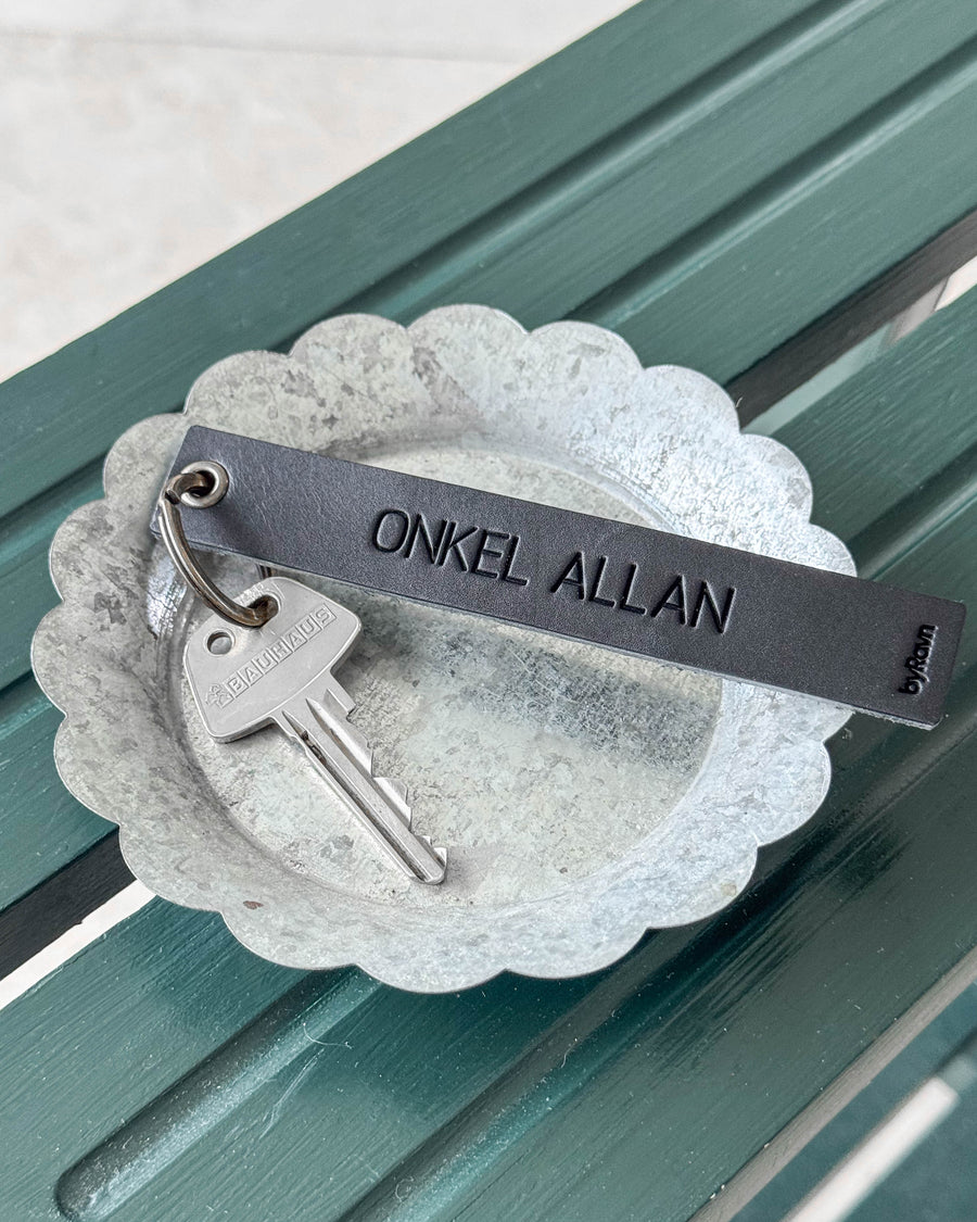 SOLO Large nyckelring i svart läder med gravyren "Onkel Allan" och nyckel i zinkskål på grön bänk