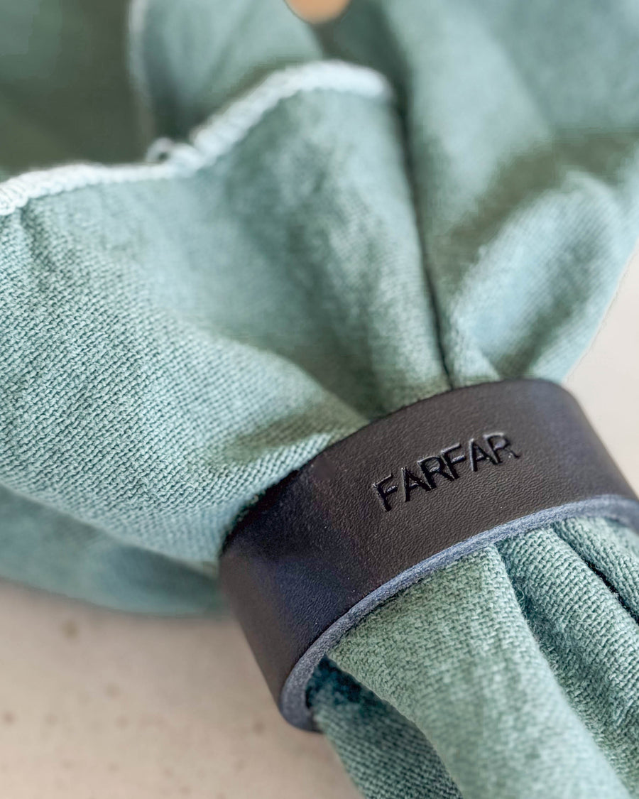 KNOT servettring i svart läder med gravyren "Farfar" runt ljusgrön tygservett