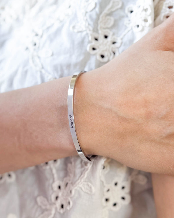 VENUS SCRIPT armband i silverfärgat rostfritt stål med namnet "Anna" ♡ i handskrift runt handleden, vit broderad blus