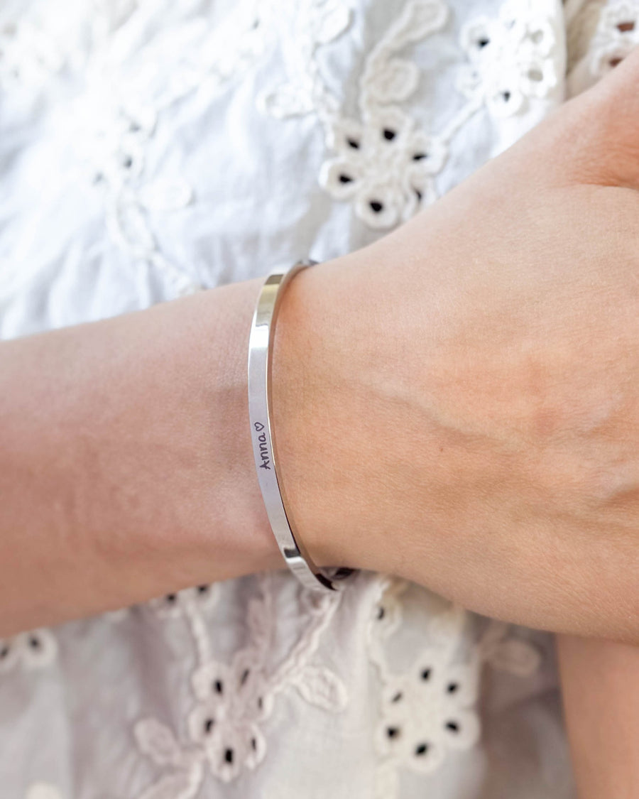 VENUS SCRIPT armband i silverfärgat rostfritt stål med namnet "Anna" ♡ i handskrift runt handleden, vit broderad blus