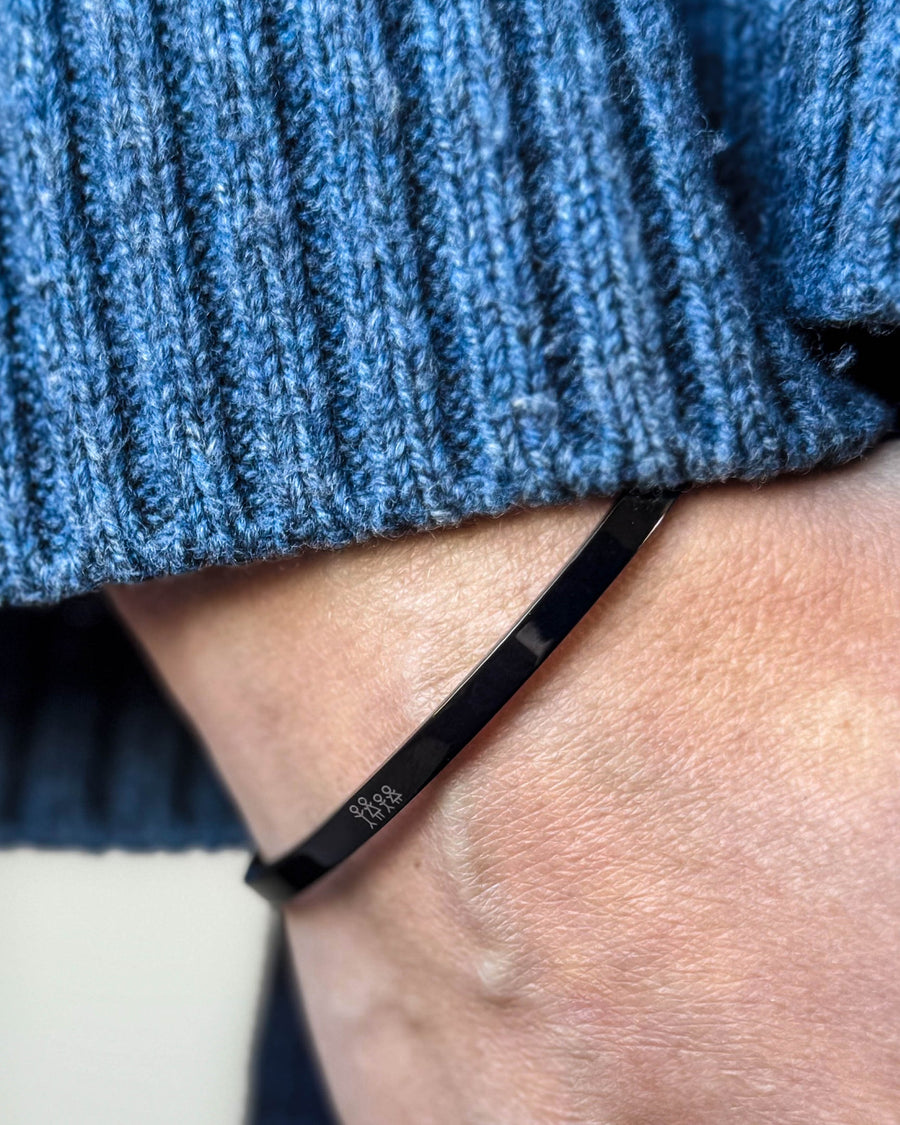 VENUS STICK armband i svart stål med graverad tändsticksfamilj runt handleden, blå ribbstickad tröja