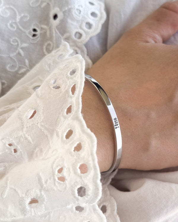 VENUS STICK armband i silverfärgat rostfritt stål med graverad tändsticksfamilj, buret till vit blus med broderi