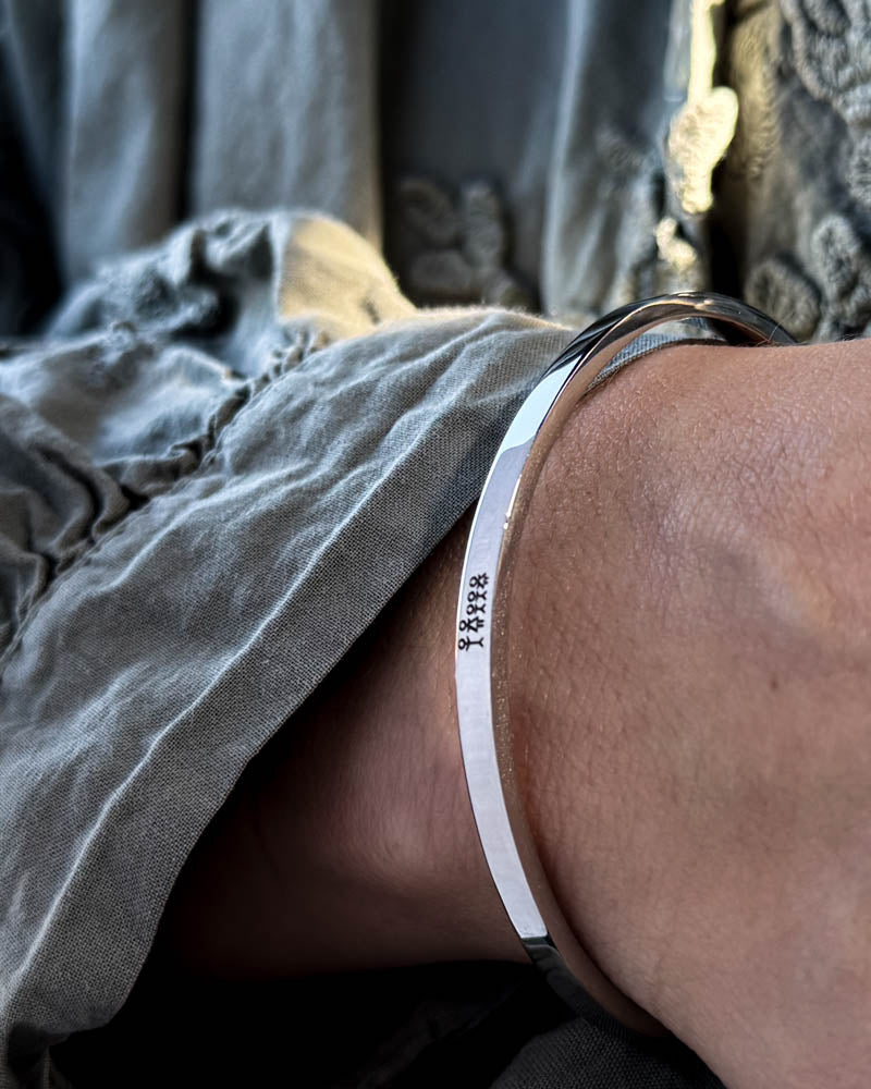 VENUS STICK armband i silverfärgat rostfritt stål med graverad tändsticksfamilj, buret till grå blus med puffärmar
